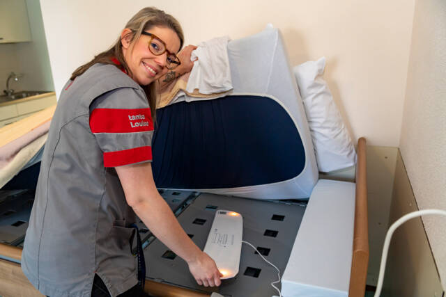 Een zorgmedewerker van tanteLouise installeert een bedsensor.
