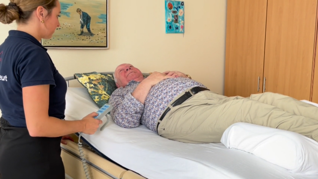 Een client ligt op bed, pratend met een ergotherapeut