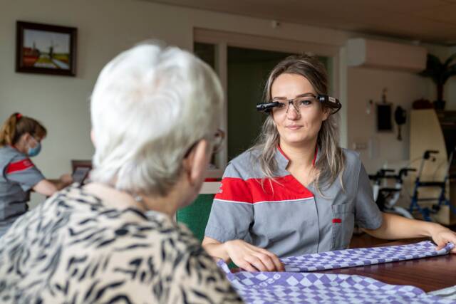 Een zorgmedewerker praat met een bewoonster terwijl ze de slimme bril draagt.
