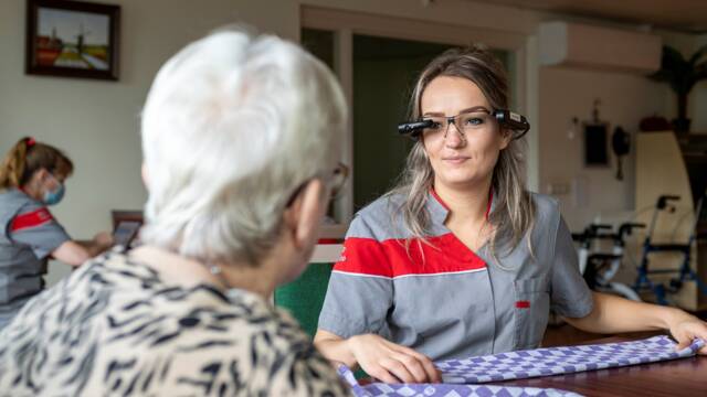 Een zorgmedewerker praat met een bewoonster terwijl ze de slimme bril draagt.